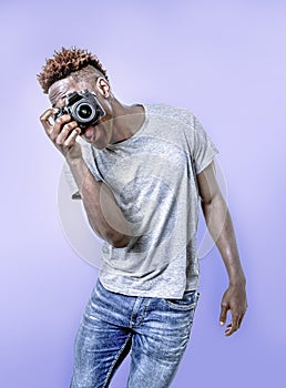 Young attractive and cool happy black afro American man holding digital reflex photo camera smiling excited background