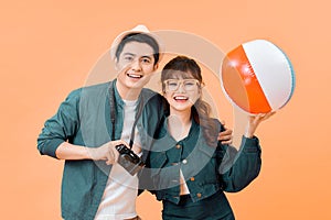 Young attractive couple with beach ball and camera on yellow background