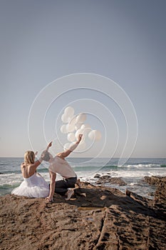 Young attractive couple at beach on rocks with white balloons
