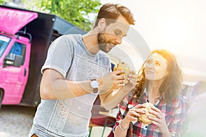 Young attractive couple eating hamburgers against food truck with lens flare in background