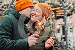 Young attractive couple hug and kiss outdoors with the sparklers in their hands celebrating New Year and Christmas. Winter