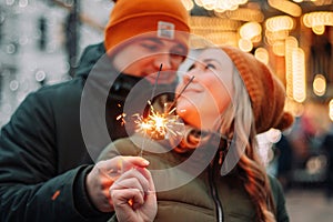 Young attractive couple hug and kiss outdoors with the sparklers in their hands celebrating New Year and Christmas. Winter