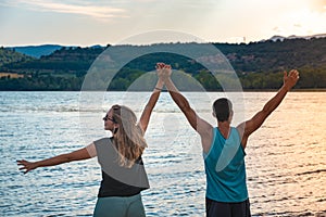 Young Attractive Couple open arms holding hands in a Beautiful Lake in summer during sunset. Discovery Travel love