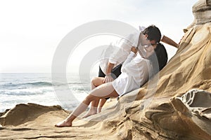 Young attractive couple sharing a kiss outdoors on beach rocks