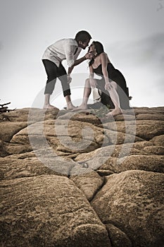 Young attractive couple sharing a moment outdoors on beach rocks