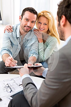 Young attractive couple signing contract with real estate agent