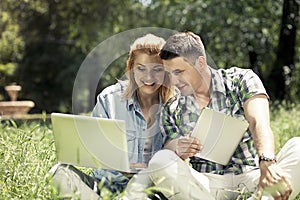 Young attractive couple sitting on the grass, looking at laptop