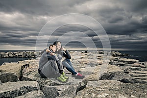 Young and attractive couple is sitting on the pier made of stones.