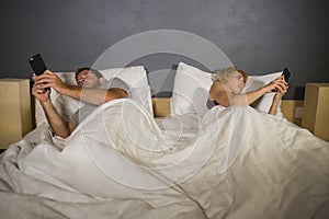 Young attractive couple using mobile phone in bed ignoring and neglecting each other obsessed networking in internet addiction and