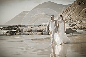 Young attractive couple walking along beach wearing white photo