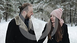 Young attractive couple walking and having fun in a winter forest under heavy snow. Man and woman in pink hat hugging