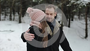 Young attractive couple walking and having fun in a winter forest under heavy snow. Man and woman in pink hat hugging