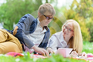 Young attractive couple wearing glasses is working or studying with laptop book note and pen lying on blanket in green