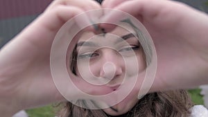 Young attractive dark haired hipster woman is smiling posing make heart shape hand gesture and looking at the camera.closeup portr