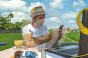 Young attractive digital nomad man working on line outdoors with laptop computer and mobile phone as freelancer and independent jo