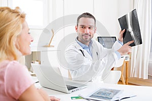 Young attractive doctor analysing X-ray with patient