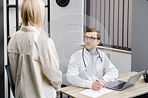 A young attractive doctor is having a consultation in his office. The doctor gives recommendations to his patient while sitting at