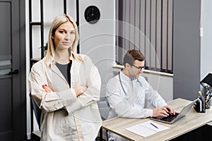 A young attractive doctor is having a consultation in his office. The doctor is making notes on the laptop, and the patient is