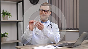 Young attractive doctor otolaryngologist sitting at his workplace in the office and holding an ear funnel in his hands