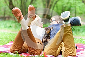 Young attractive european couple with small dog between them is getting rest on blanket in some summer park at warm sunny day.