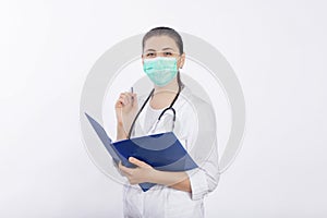 A young, attractive female doctor in a white coat and mask holds a folder in her hands and fills out a medical document.