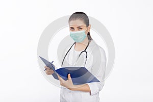 A young, attractive female doctor in a white coat and mask holds a folder in her hands and fills out a medical document.