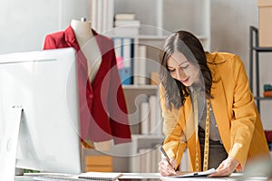 Young attractive female fashion designer sketching idea on paper at desk, working with a laptop at home