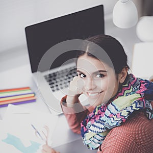 Young attractive female fashion designer working at office desk, drawing while talking on mobile