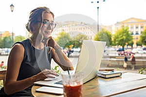 Young attractive female in fashionable spectacles having online training course via portable laptop computer