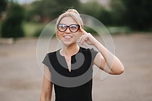 Young attractive female techer in black dress with sunglasses standing outside. Background of school