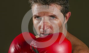 Young attractive and fierce looking man in boxing gloves posing in defense boxer stance isolated on dark background in sport and