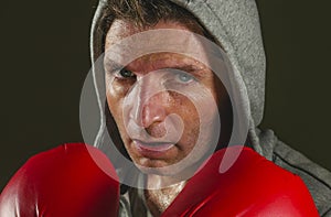 Young attractive and fierce looking man in boxing gloves posing in defense boxer stance isolated on dark background in sport and