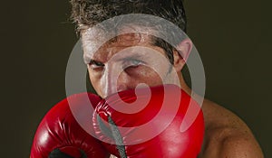 Young attractive and fierce looking man in boxing gloves posing in defense boxer stance isolated on dark background in sport and