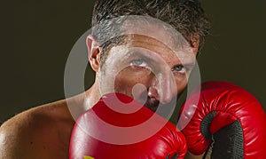 Young attractive and fierce looking man in boxing gloves posing in defense boxer stance isolated on dark background in sport and