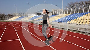 Young attractive fit active woman jumping with skipping rope working out warming up at big stadium on sunny spring day