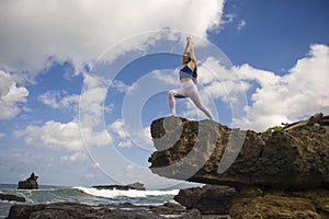 Young attractive and fit woman practicing acroyoga balance exercise and yoga meditation at beautiful beach rock cliff in healthy