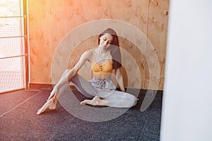 Young attractive fitness girl sitting on the floor near the window on the background of a wooden wall, resting on yoga classes