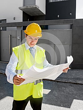 Young attractive foreman worker supervising building blueprints outdoors wearing construction helmet