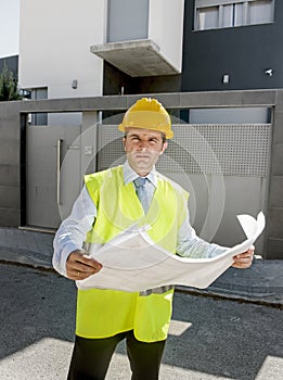 Young attractive foreman worker supervising building blueprints outdoors wearing construction helmet