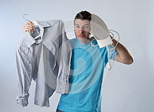 Young attractive and frustrated man holding iron and shirt stressed and tired in bored and lazy face