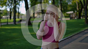 Young attractive girl athlete suffering from a very severe headache. Woman jogging in the park. 4K