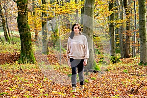 Young attractive girl in beige sweater and black jeans walks through a leafy colorful autumn forest in Bavaria, Germany