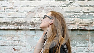 Young attractive girl in black t-shirt and sunglasses in rock style on urban background listening to music