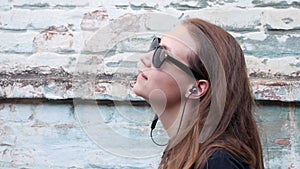 Young attractive girl in black t-shirt and sunglasses in rock style on urban background listening to music