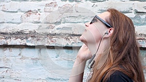 Young attractive girl in black t-shirt and sunglasses in rock style on urban background listening to music