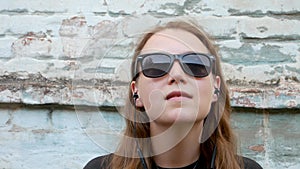 Young attractive girl in black t-shirt and sunglasses in rock style on urban background listening to music