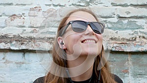 Young attractive girl in black t-shirt and sunglasses in rock style on urban background listening to music