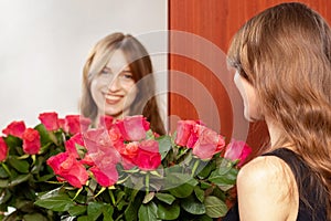 Young attractive girl with a bouquet of red roses is reflected in the mirror