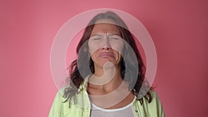 Young attractive girl desperately crying on a pink wall background