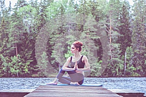 Young attractive girl doing Half lord of the fishes exercise, Ardha Matsyendrasana pose with namaste  on the lake. The concept of
